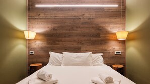 A hotel room with a wooden headboard, two bedside lamps, a bed with white linens, and two round wooden side tables.