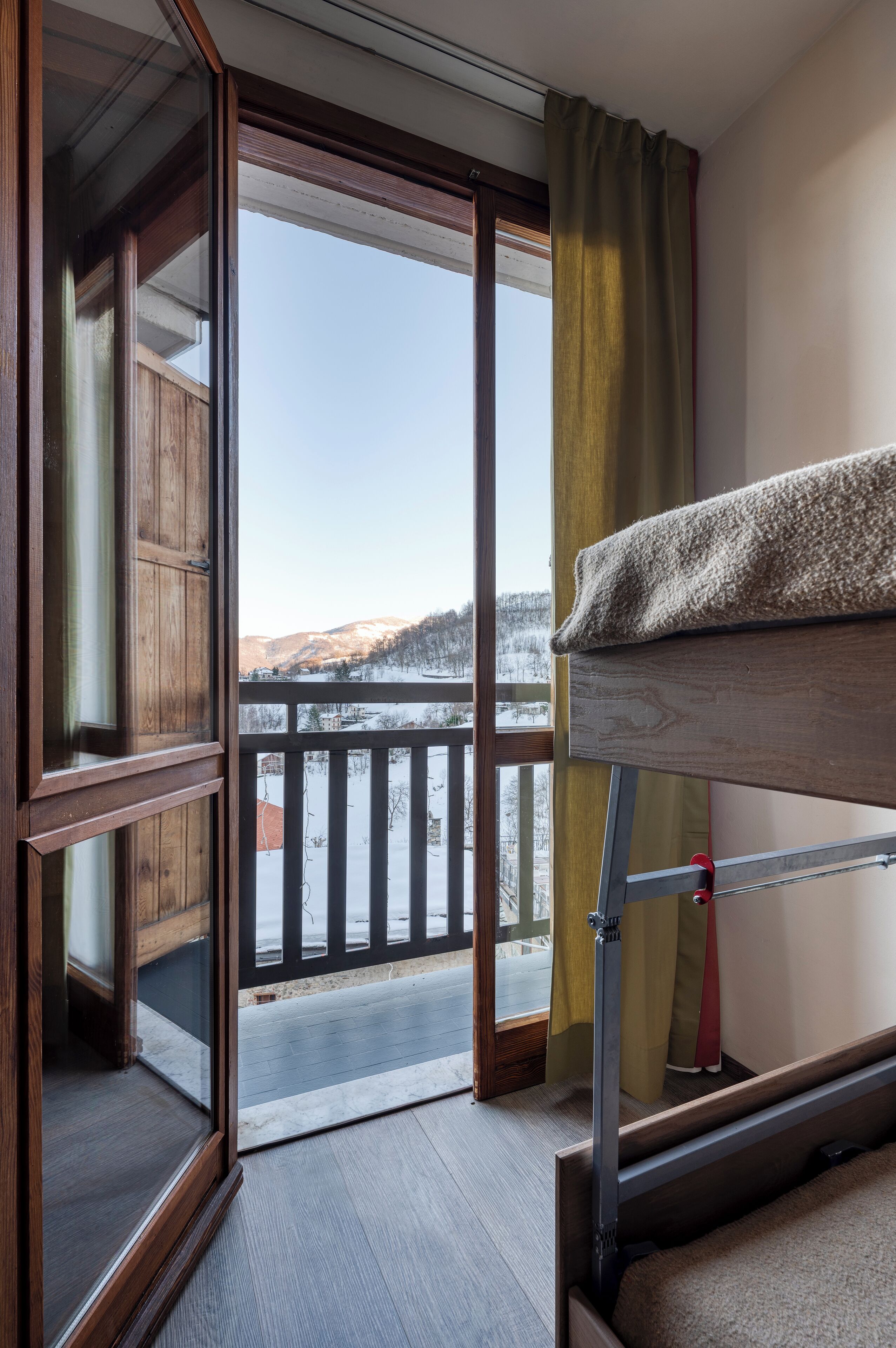 A room with a wooden bunk bed, a sliding glass door leading to a balcony with a view of snow-covered hills.