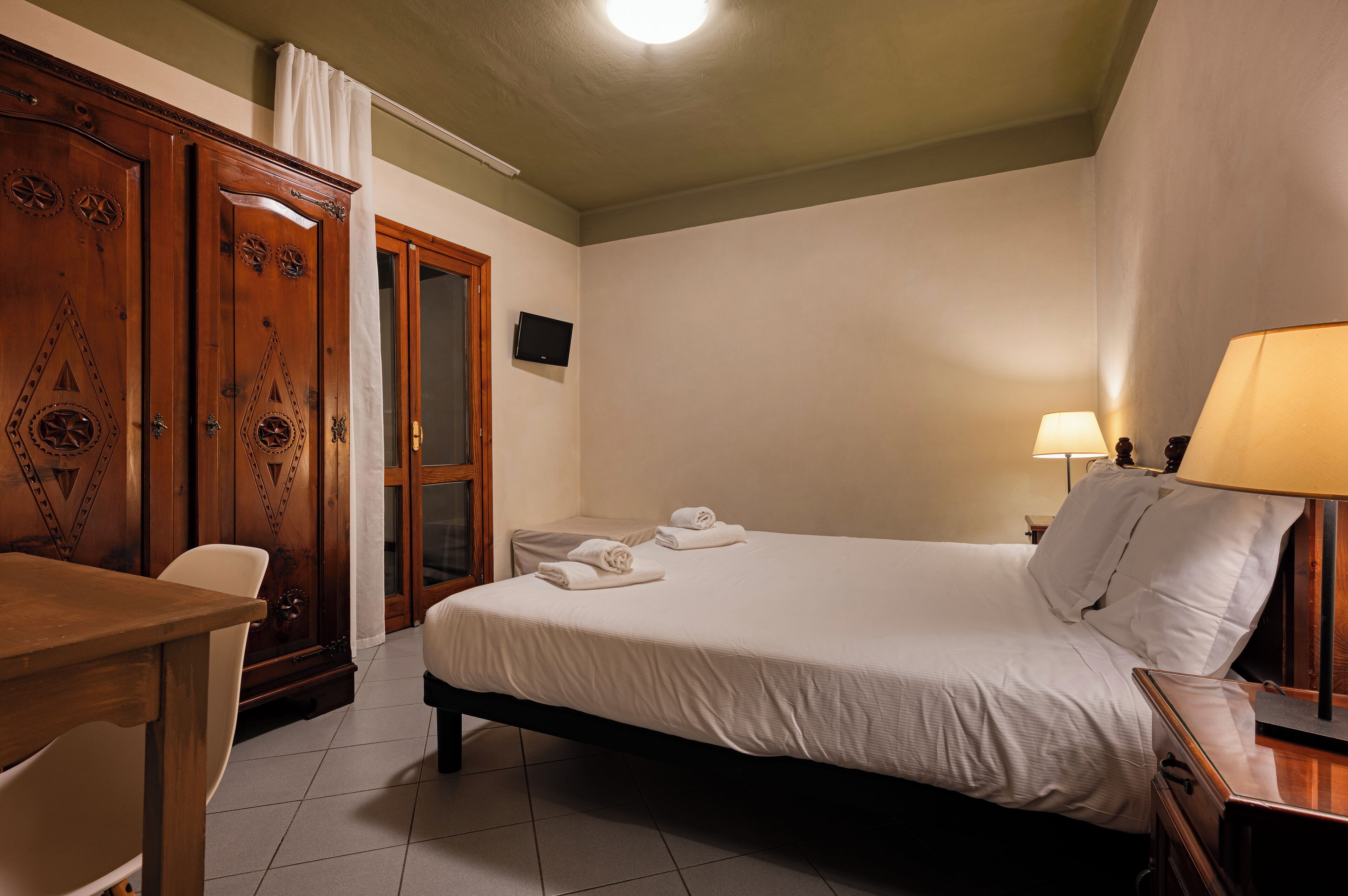 A hotel room with a bed, a desk, a chair, a television, and a lamp.