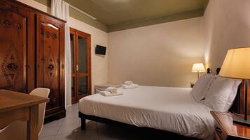 A hotel room with a bed, a desk, a chair, a television, and a lamp.