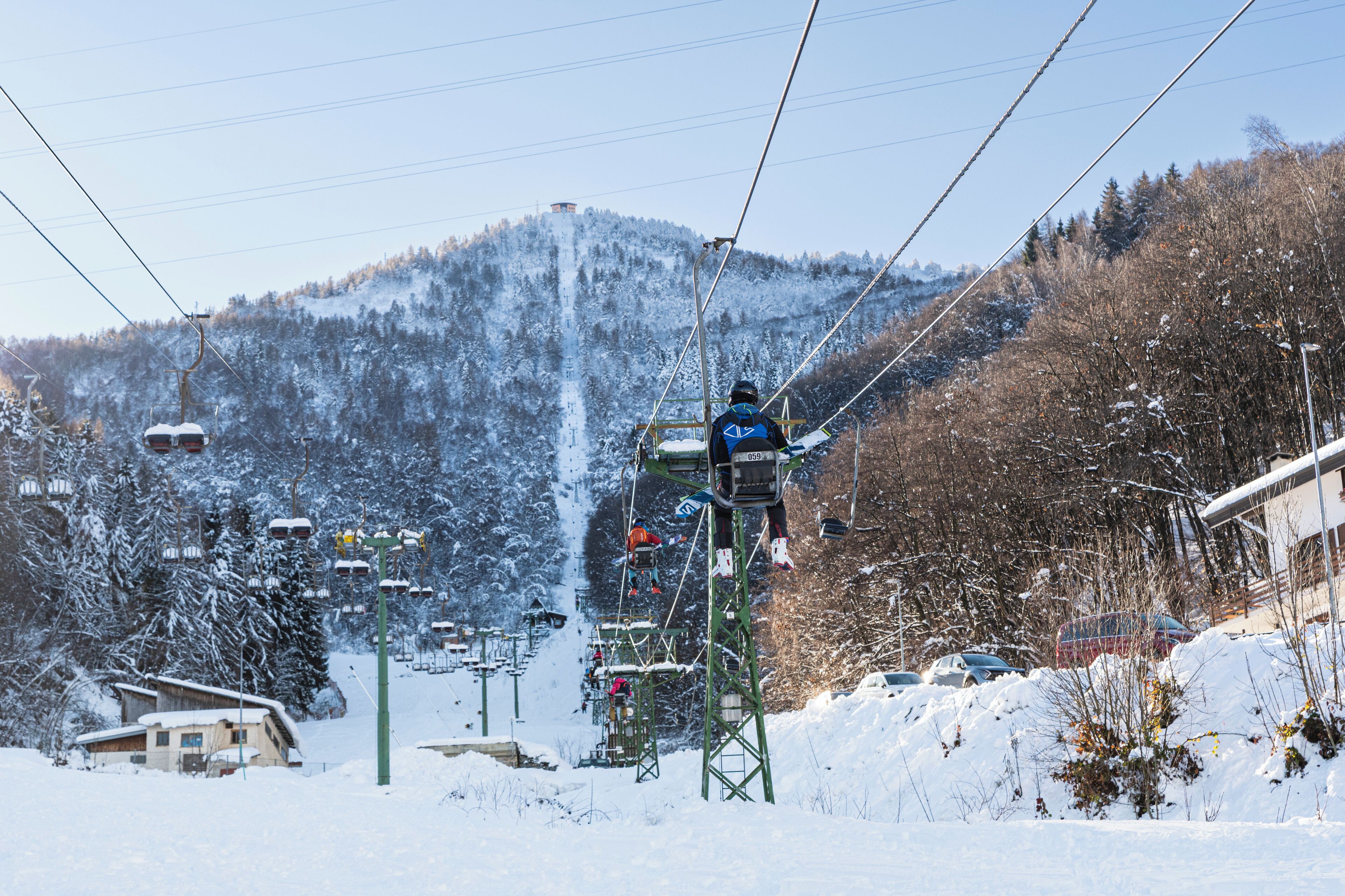 Una seggiovia con cabine, con una montagna innevata sullo sfondo e cielo sereno.