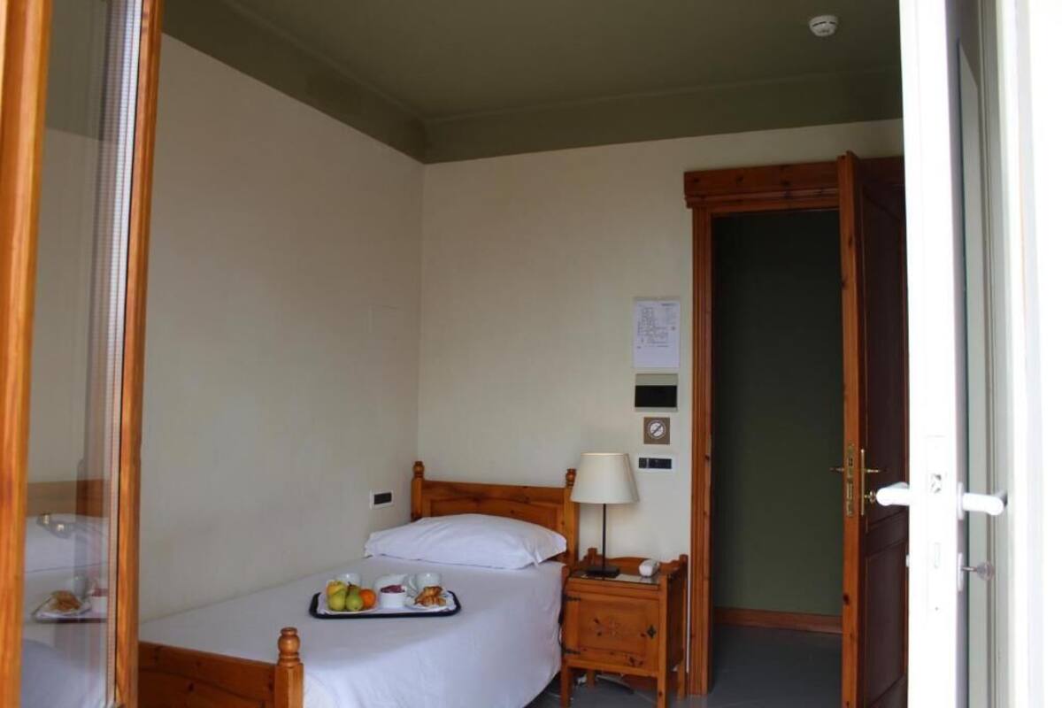 Une chambre d’hôtel avec un lit simple, une table de chevet avec une lampe et un plateau contenant des articles pour le petit-déjeuner.