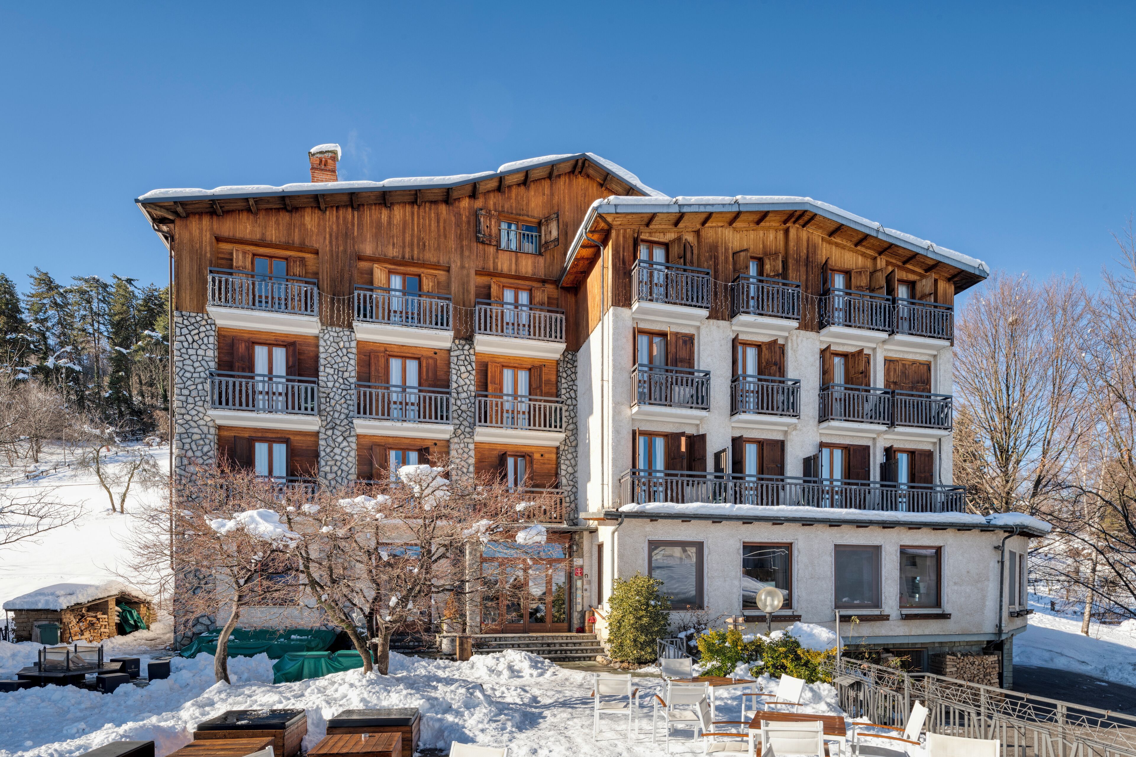 A multi-story wooden building with balconies, stone accents, and a snow-covered landscape.