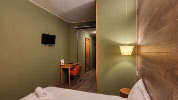 Quarto de hotel com cama, escrivaninha com cadeira, televisão e cabeceira de madeira.
