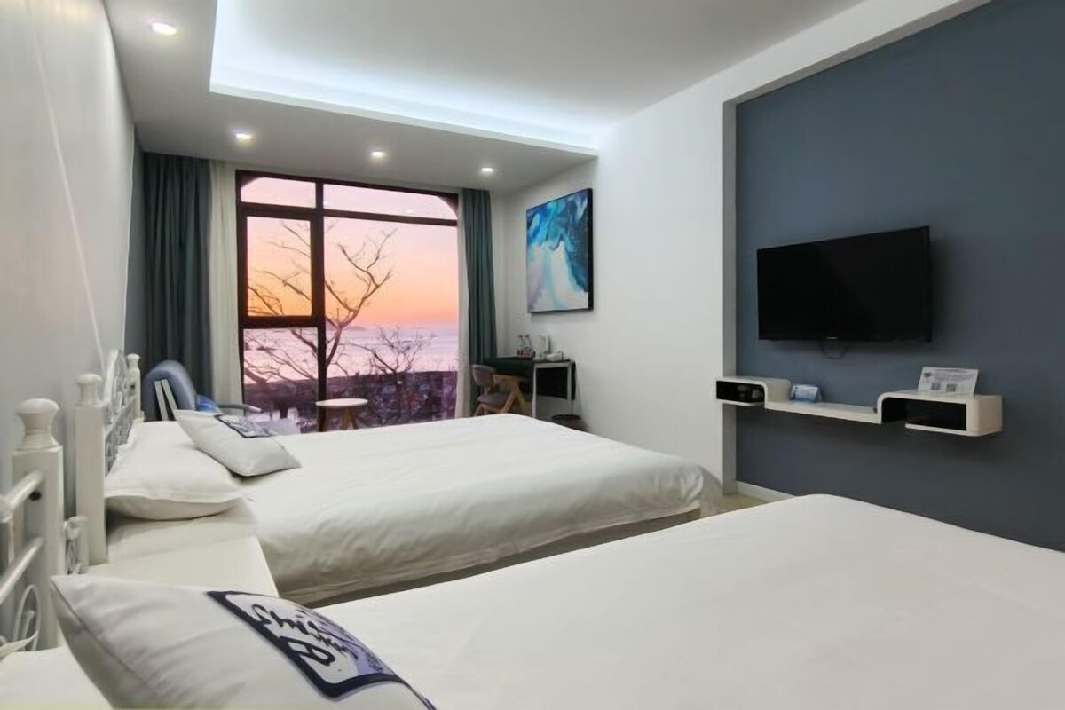 A hotel room with two beds, a large window with a view, a flat-screen TV, and a desk with a chair.