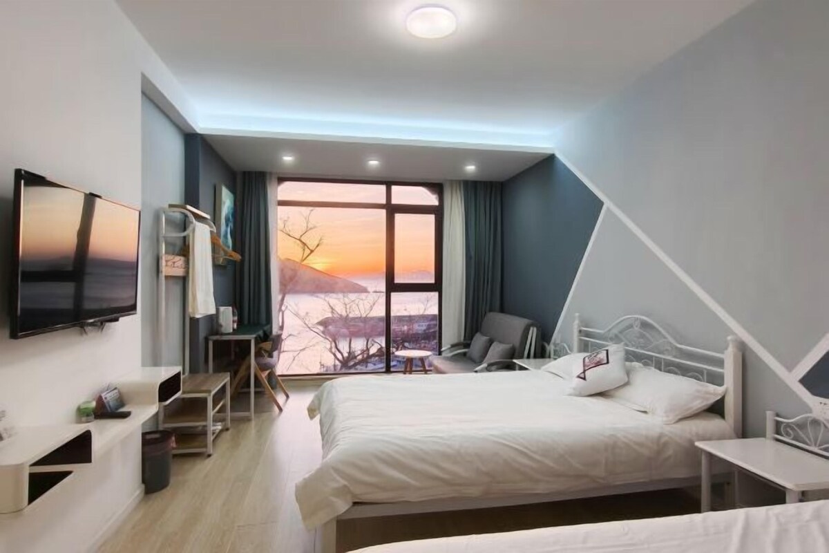 A modern hotel room with a large window, a bed, a desk, and a TV.