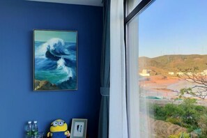 A room with a large window, a framed ocean wave painting, a Minion plush toy, and a framed picture on the wall. - Xihai Hostel (Shengsi)