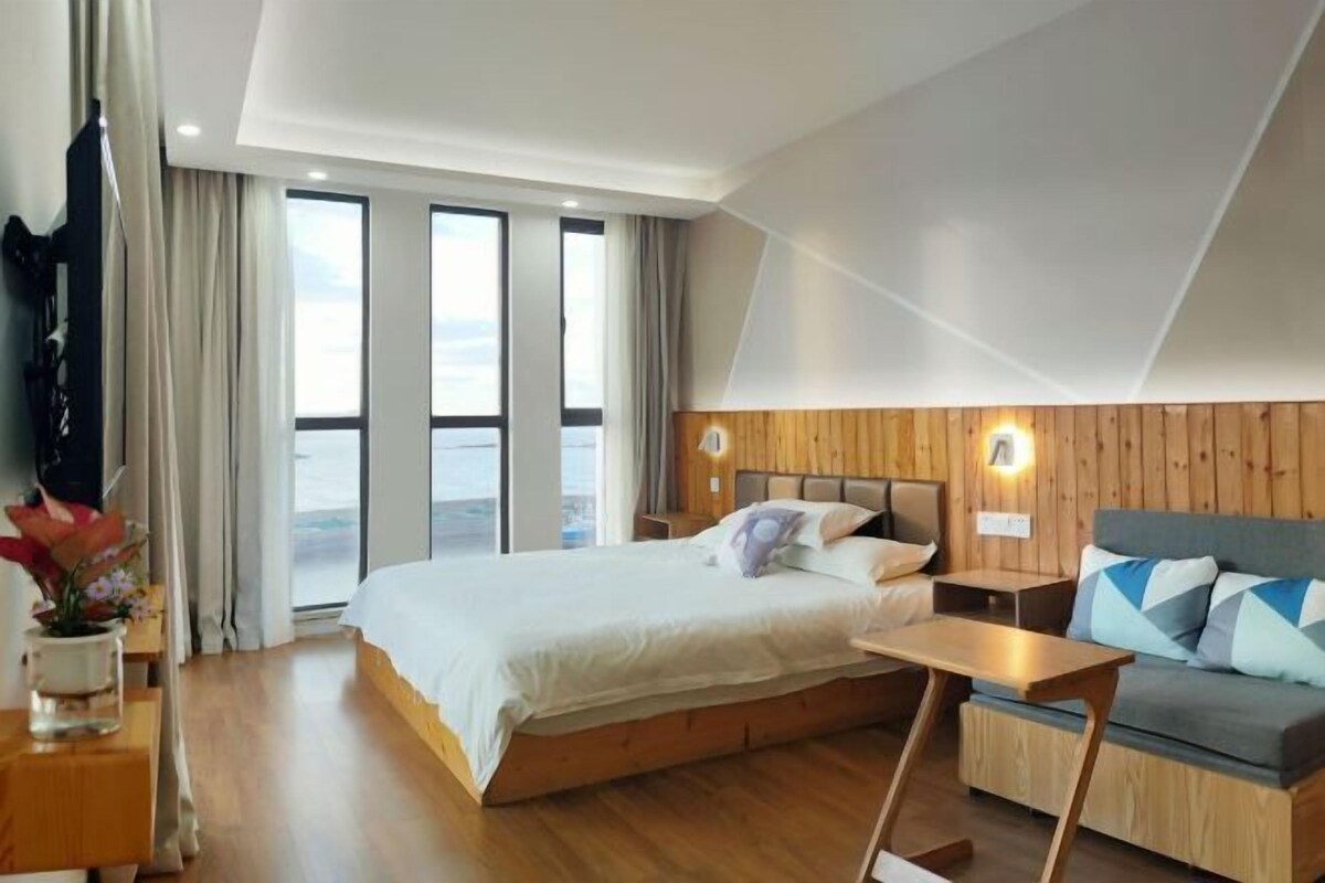 A modern hotel room with a large bed, a sofa, a small table, and a view of the outdoors.