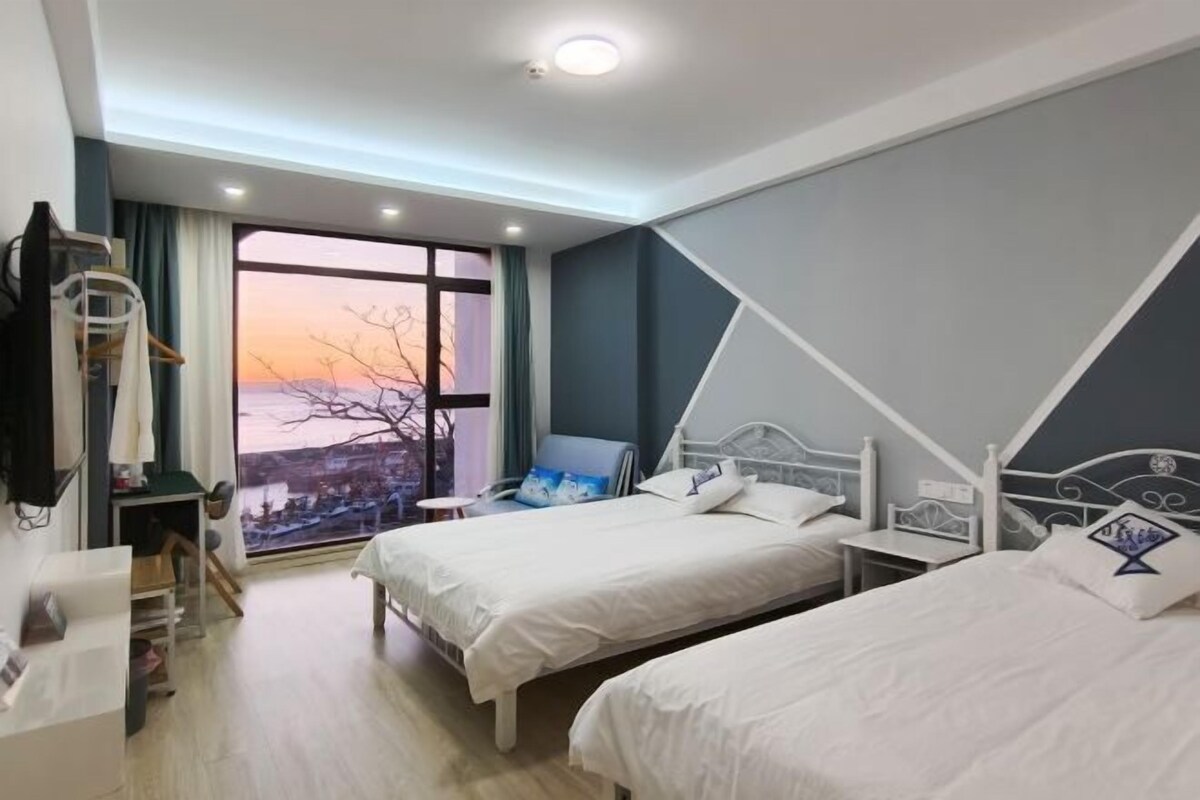 A hotel room with two beds, a desk, a chair, and a large window with a view.