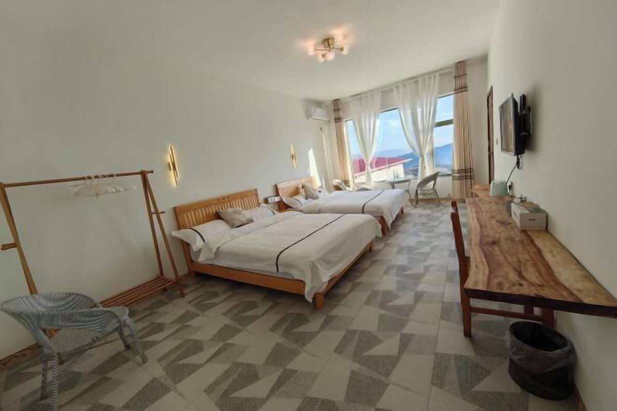 A hotel room with two beds, a wooden desk, a chair, a TV, and a view of the mountains.