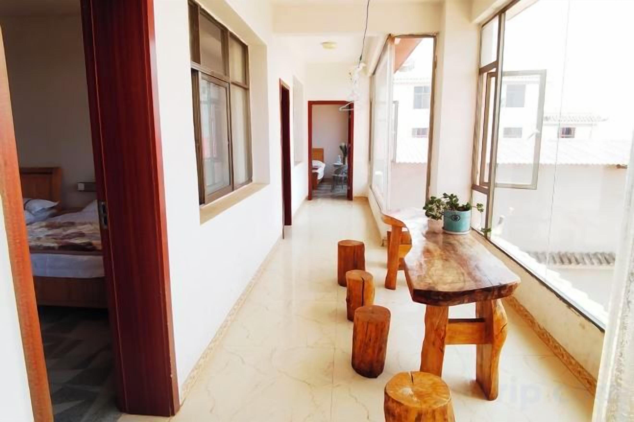 Un pasillo con una mesa de madera, taburetes, una cama y un ventanal con vistas.