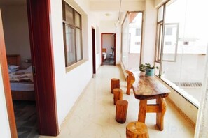 A corridor with a wooden table and stools, a bed, and a window with a view. - Kunming Red Earth Summer Homestay (Kunming)