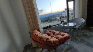 A modern room with a large window, a brown cushioned chair, a round glass table, and a wicker chair.