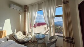 A hotel room with a bed, two chairs, a small table, and a window with curtains.