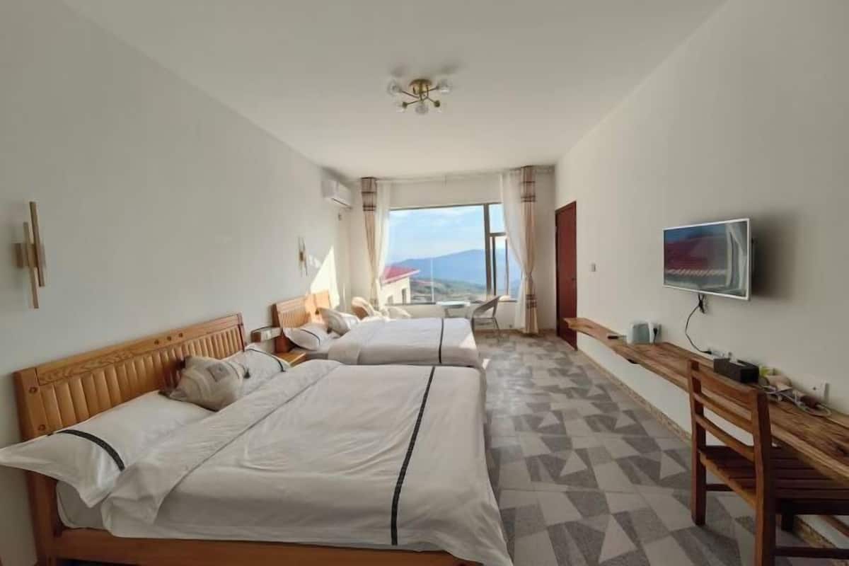A hotel room with two beds, a TV, a wooden desk, and a view of the mountains.