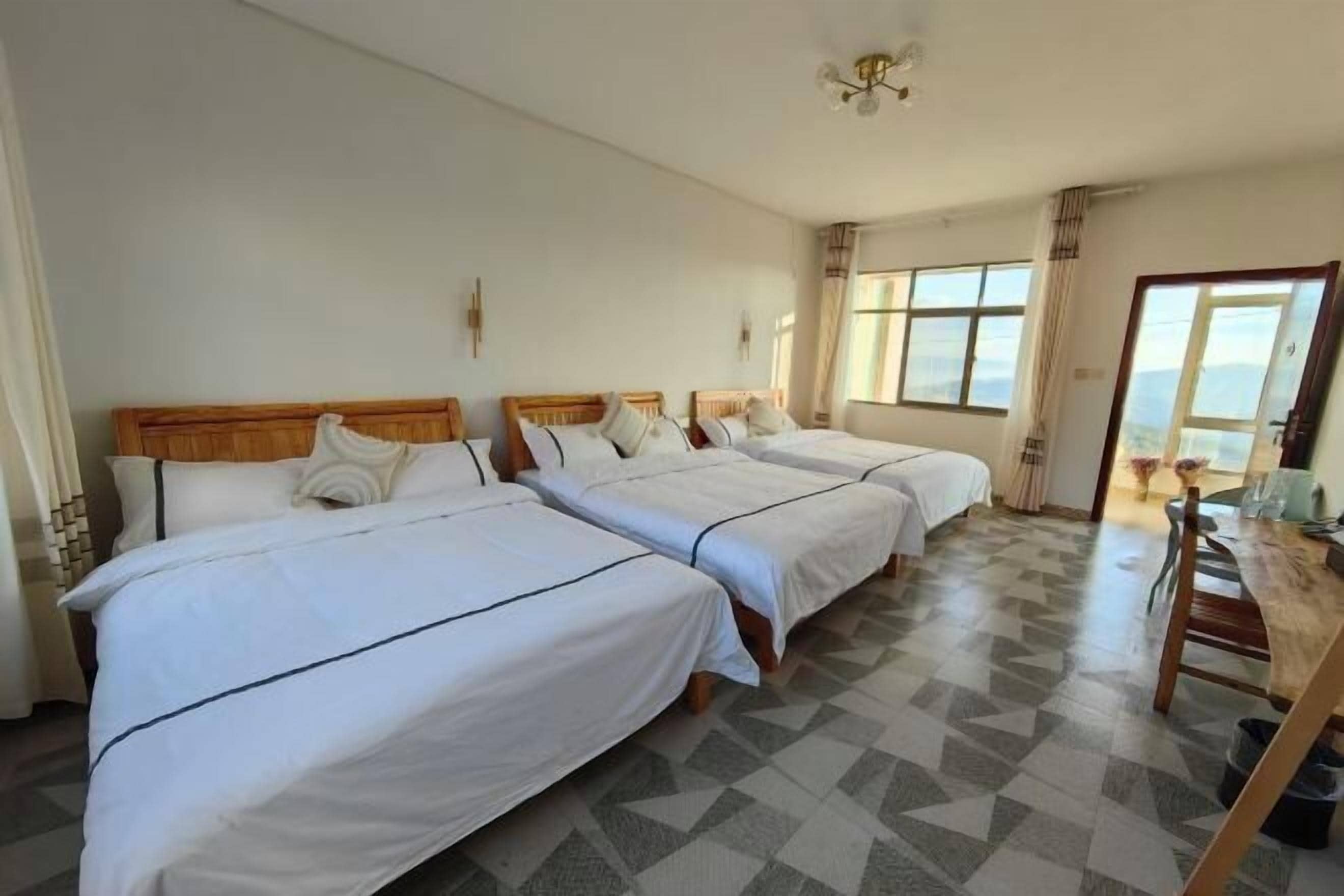 Habitación de hotel con tres camas, cabecera de madera, una mesa de comedor y vista al exterior.