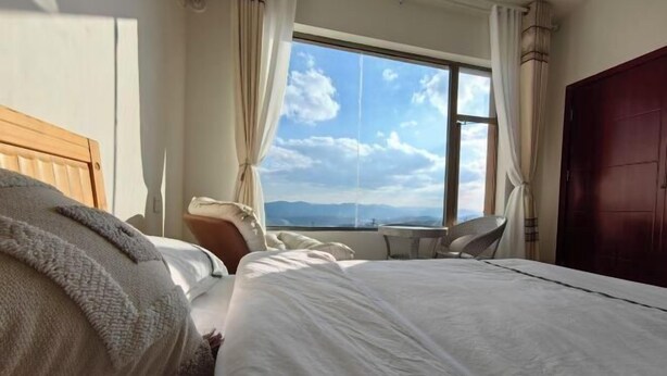 A hotel room with a large bed, a small table, and a view of the mountains through a window.