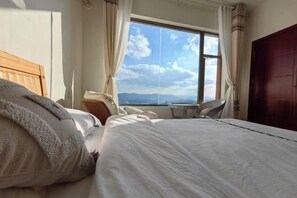 Habitación de hotel con una cama grande, una mesita y vistas a las montañas desde la ventana.
