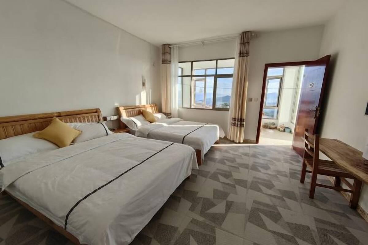 A hotel room with two beds, a wooden bench, and a large window offering a view.