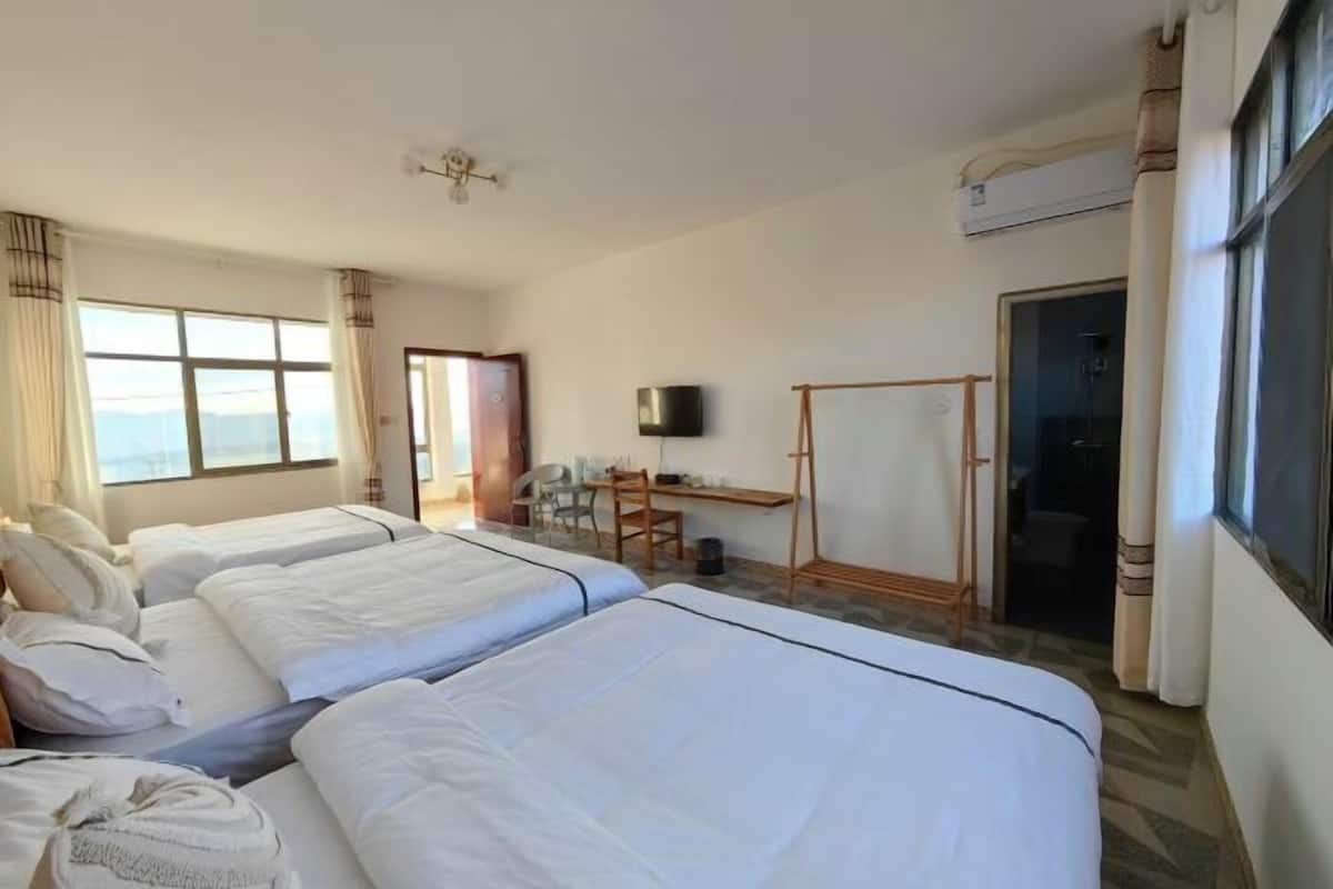 A hotel room with three beds, a desk, a chair, a TV, and a view of the mountains.