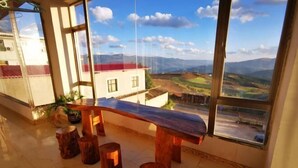 A room with a large window overlooking a scenic landscape, a wooden bench, and a tiled floor.