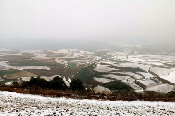 Vista panorámica de un paisaje nevado con campos en terrazas y un pueblo lejano.