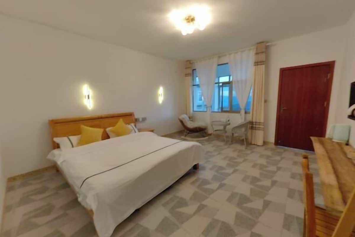 A bedroom with a bed, a desk, a chair, a TV, and a door.