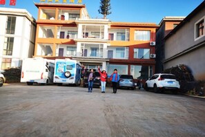 A building with multiple floors, a parking area with vehicles, and a group of people standing in the foreground. - Kunming Red Earth Summer Homestay (Kunming)