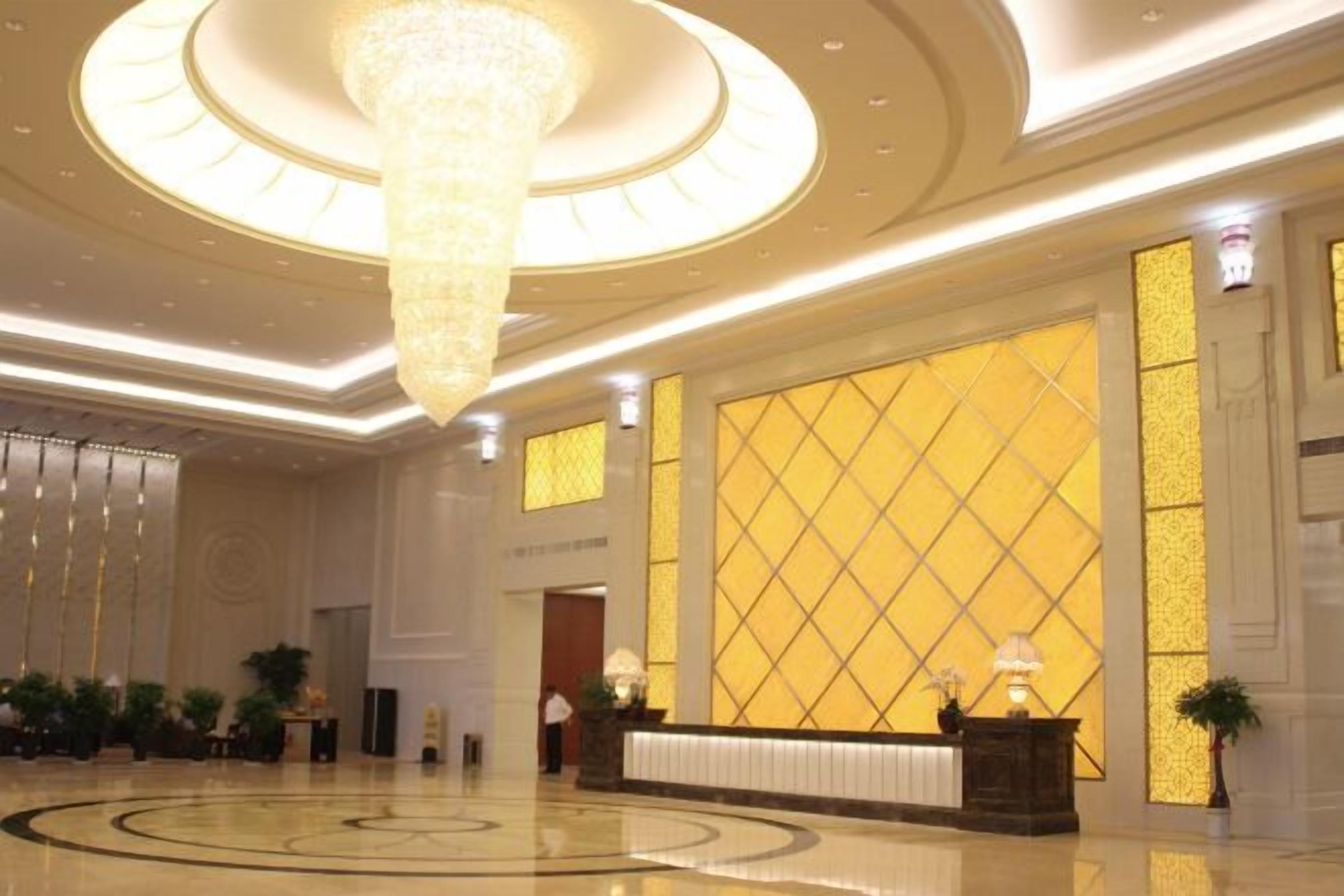 A spacious lobby with a large chandelier, a reception desk, and a patterned wall.