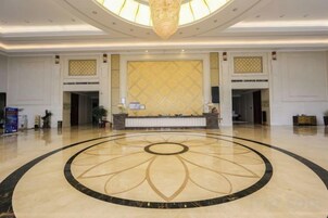 A spacious lobby with a central reception desk, a large chandelier, and a decorative floor pattern.