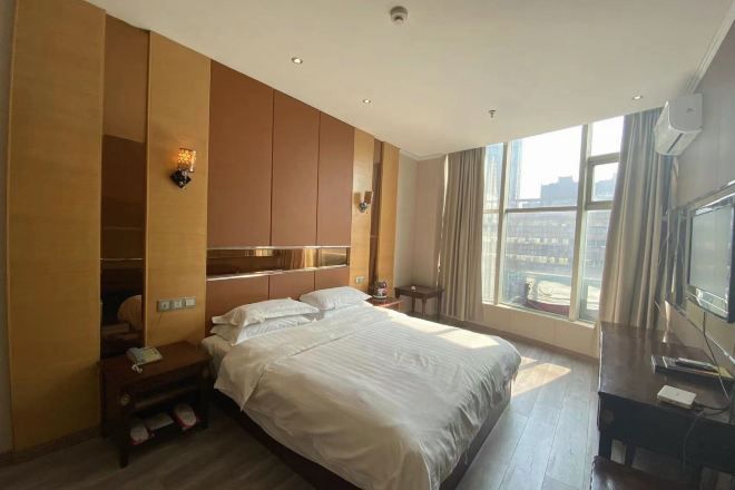 Habitación de hotel con una cama grande, armario empotrado, televisor y ventana con vistas a la ciudad.