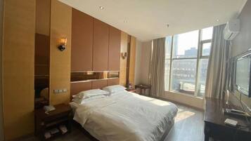 Habitación de hotel con una cama grande, armario empotrado, televisor y ventana con vistas a la ciudad.