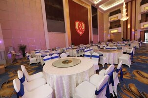 A banquet hall with round tables, white chairs, and blue sashes.