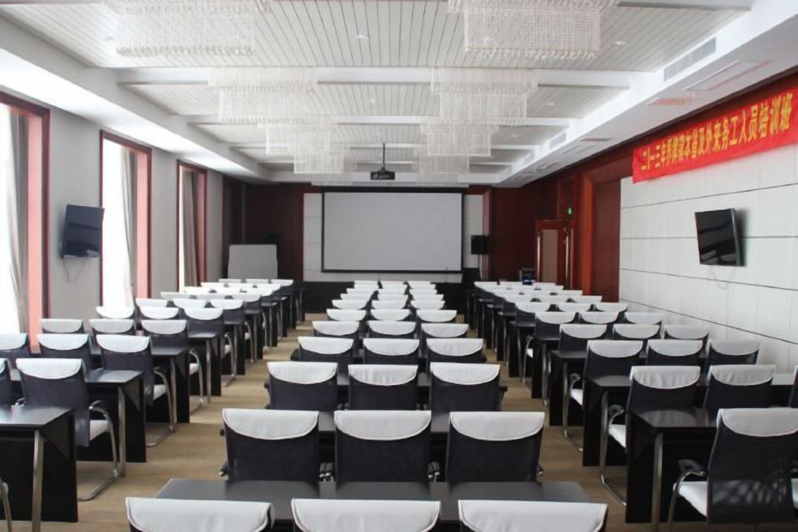 A conference room with rows of tables and chairs, a projector screen, and a whiteboard.