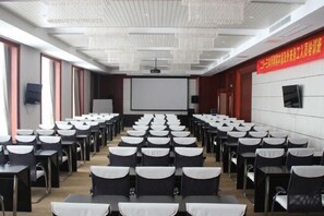 A conference room with rows of tables and chairs, a projector screen, and a whiteboard. - Dongjiang Holiday Hotel (Danyang)