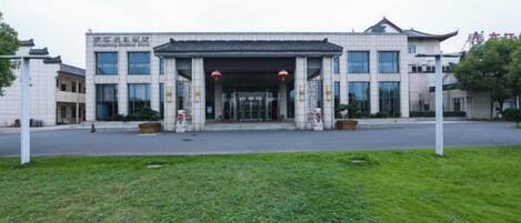 A modern building with a traditional architectural style, featuring a large entrance with a covered walkway, surrounded by a well-maintained lawn.