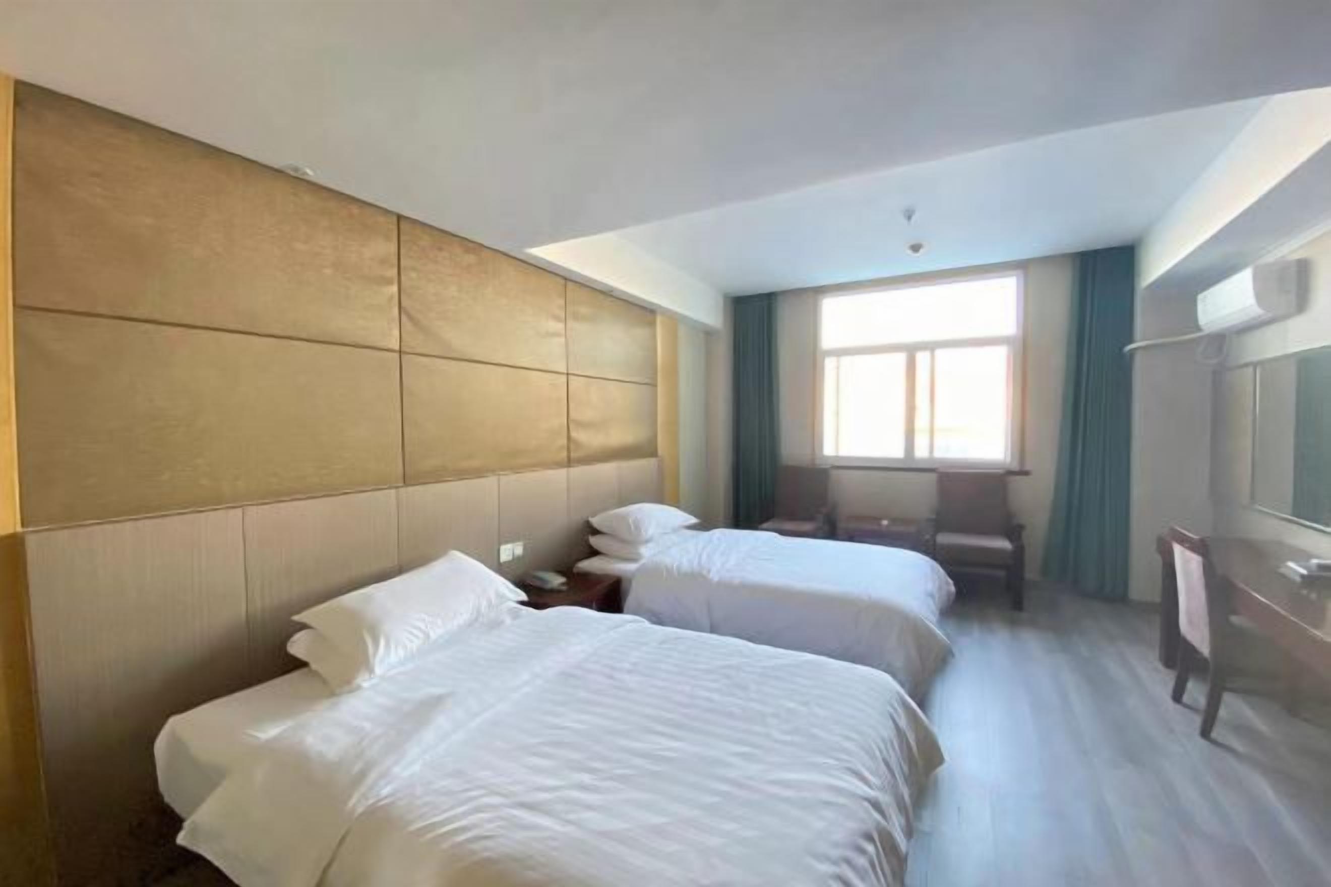 A hotel room with two beds, a large window, a mirror, and a wooden headboard.