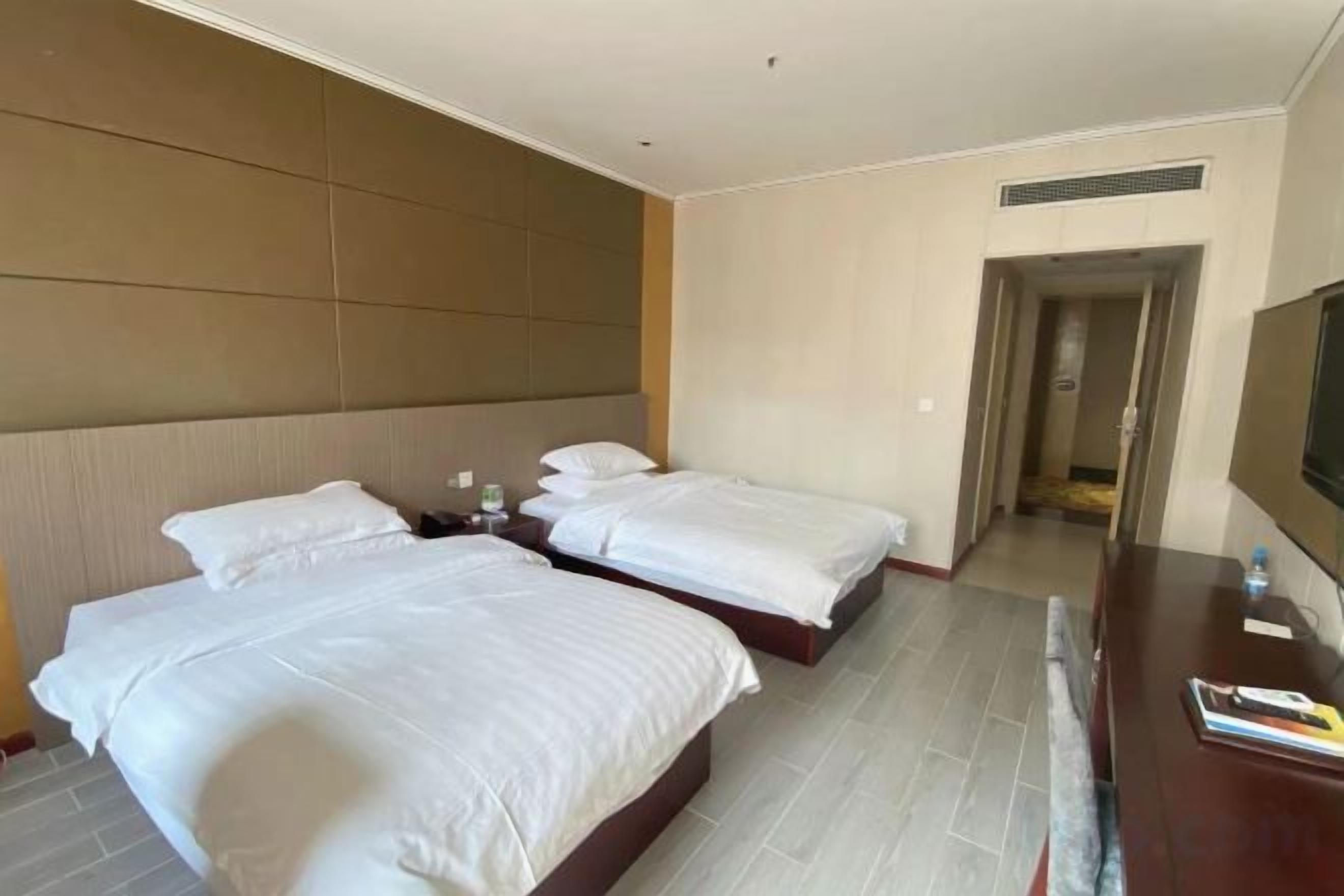 Une chambre d’hôtel avec deux lits, un téléviseur à écran plat et une commode en bois.