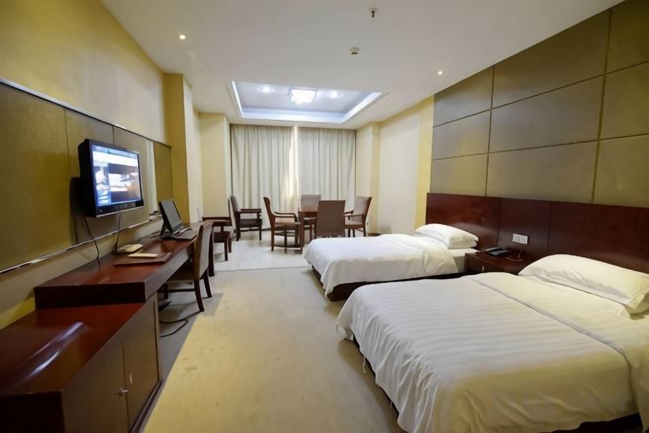 A hotel room with two beds, a desk with a computer, a TV, and a large window with curtains.