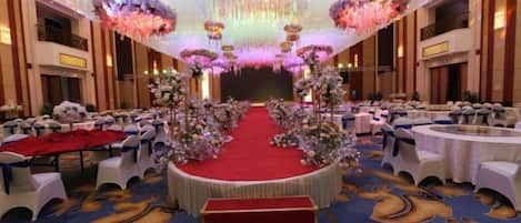 A banquet hall with a central stage, round tables, and a red carpet.