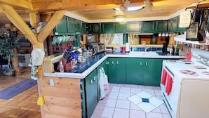 Eine rustikale Küche mit Holzbalken, grünen Schränken, Fliesenboden und einem weißen Herd.