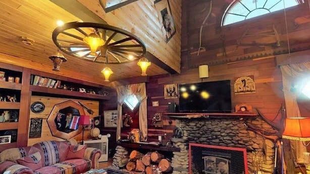 Ein gemütliches Wohnzimmer mit Kamin, Holzwänden, einem großen Fernseher und einem außergewöhnlichen Deckengestalt.