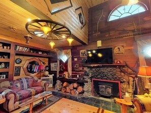 Una sala de estar acogedora con chimenea, paredes de madera, un televisor grande y un diseño de techo único.