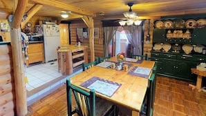 Ein Holzblockhaus-Innenraum mit Esstisch, Stühlen, einer Küchenzeile und einer Deckenleuchte.
