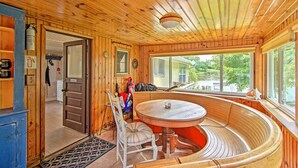 A wooden cabin interior with a round table and bench, a door leading to another room, and a window with a view of greenery outside. - Horicon Riverfront Retreat w/ Deck, Dock + Patio (Horicon)