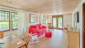 A spacious room with a wooden ceiling, a red sofa, a wooden dining table, and a rocking chair. - Horicon Riverfront Retreat w/ Deck, Dock + Patio (Horicon)