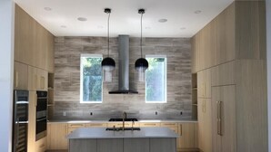 A modern kitchen with a central island, built-in ovens, and pendant lighting.