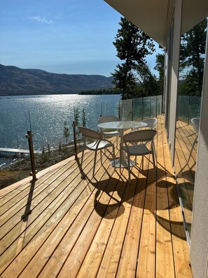 Une terrasse en bois dotée d’une balustrade en verre, qui offre une vue sur un lac.