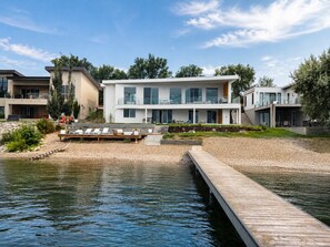 A modern waterfront property with a wooden dock, a pool, and a landscaped garden.