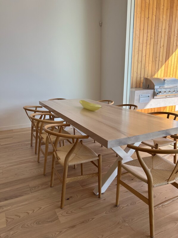 A dining area with a wooden table and chairs, a yellow bowl on the table, and a built-in grill in the background.